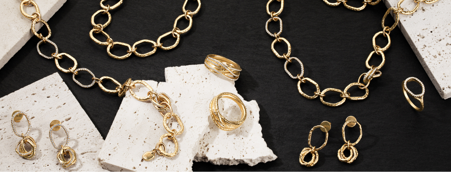 Gold jewelry set including necklaces, bracelets, and rings on a textured surface.